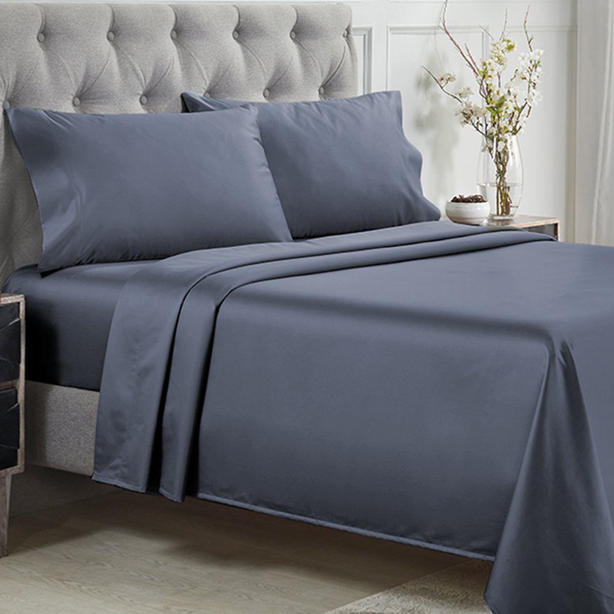 Made bed with smooth, dark blue 1000 thread count cotton sateen sheet set with a tufted headboard.
