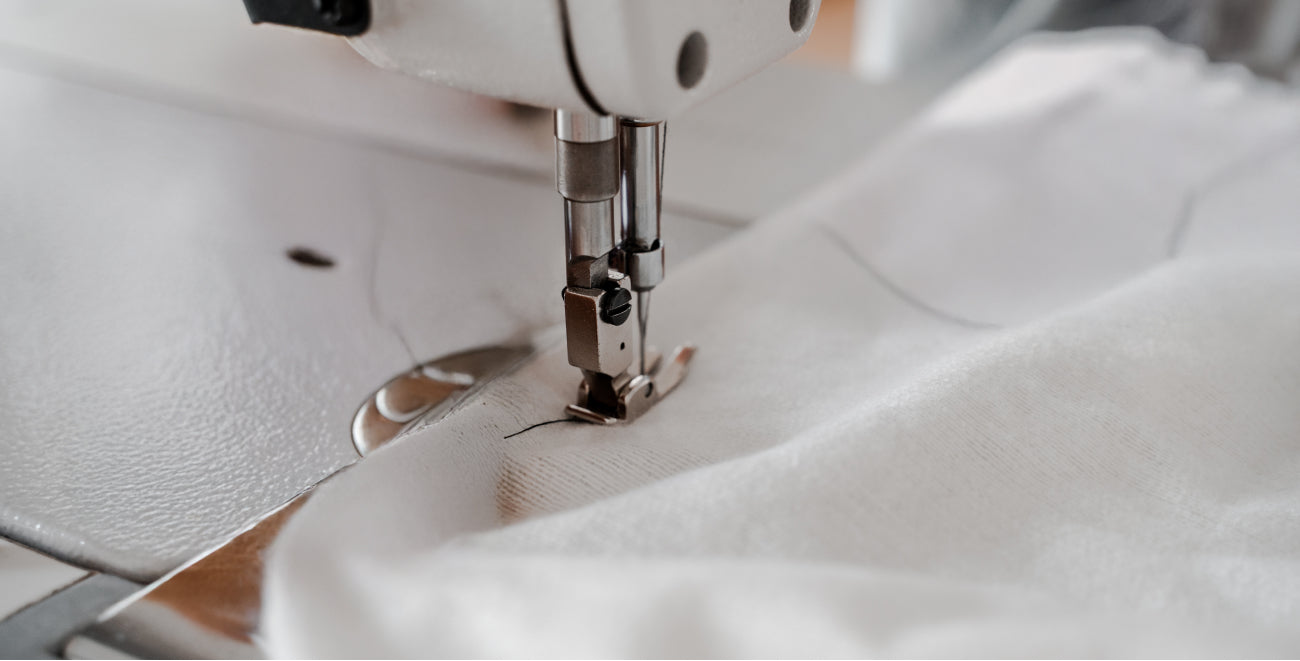 Close-up of a commercial sewing machine needle stitching a 100% white cotton stitch bedding set.