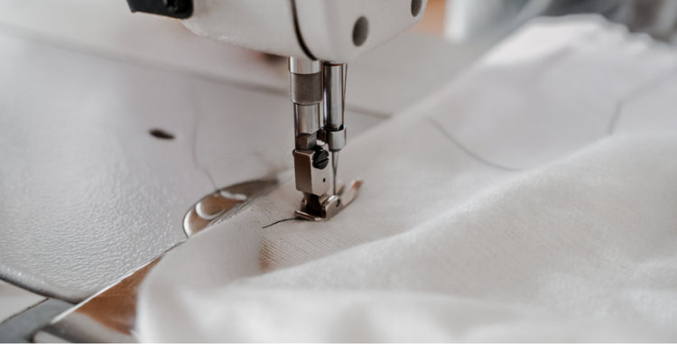 Close-up of a commercial sewing machine needle stitching a 100% white cotton stitch bedding set.