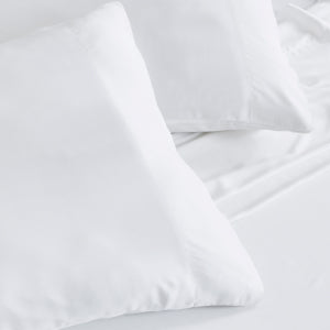 Close-up of two smooth, bright white cotton pillow cases and pillow covers on a fresh bed by CDD.