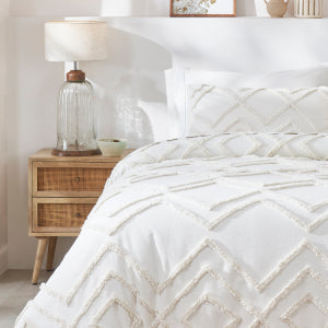 White textured comforter & duvet cover with pattern on the bed with a wooden nightstand and lamp.